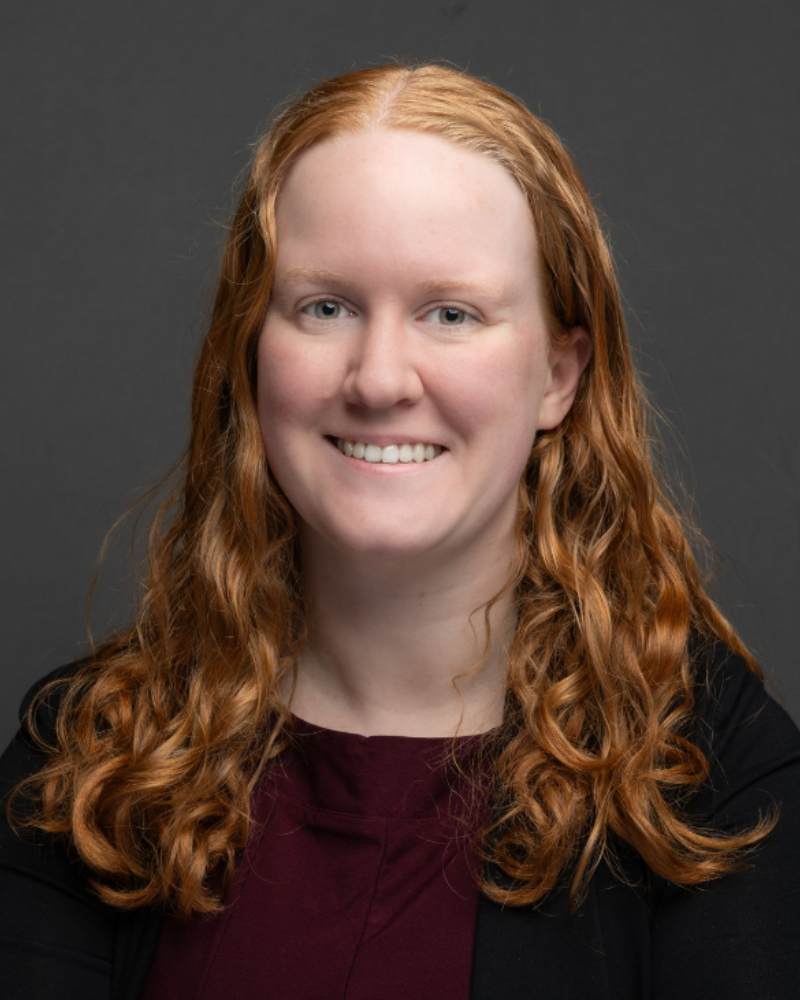 Woman with long red hair smiling against a gray background